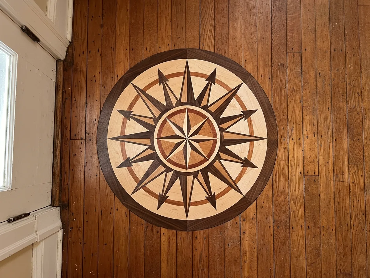 Round wood compass rose medallion of several contrasting species set flush into an oak strip floor in an entry hall